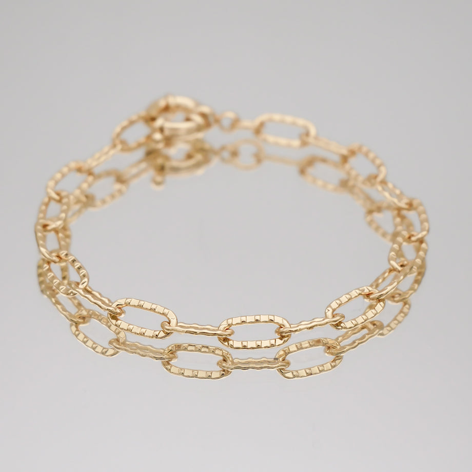 Gold chain link bracelet on reflective surface.