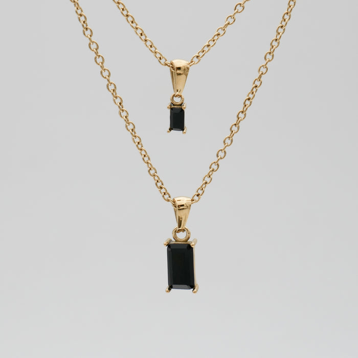 Two gold necklaces with black rectangular pendants.