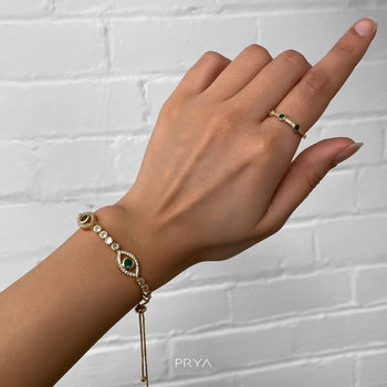 Model wearing Gold Evil Suspended bracelet paved with CZ diamonds and Emerald Green Gem