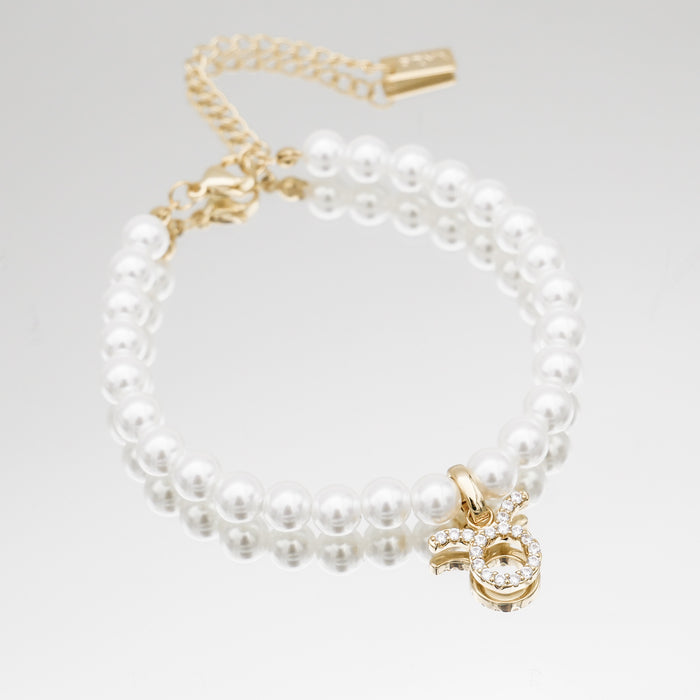 Gold-accented pearl bracelet with zodiac charm.