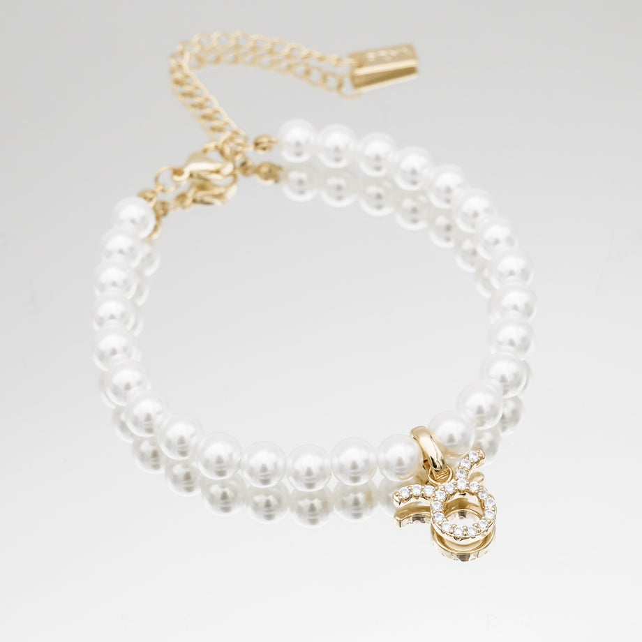 Gold-accented pearl bracelet with zodiac charm.