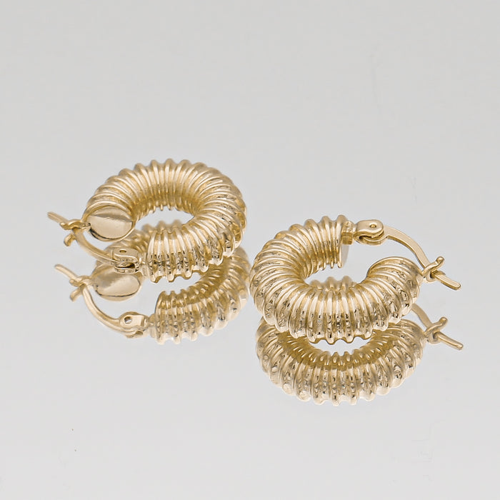 Gold ribbed hoop earrings on reflective surface.