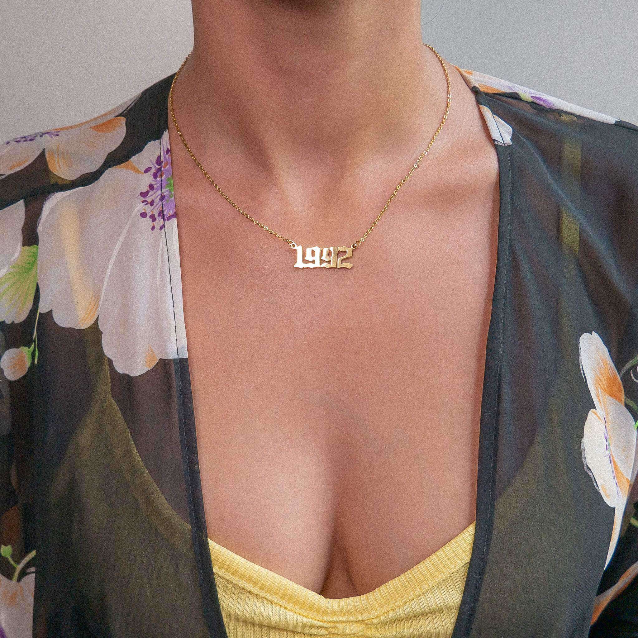 Woman wearing a yellow strappy top and flowery see-through cardigan sporting a 1993 gold birth year chain necklace