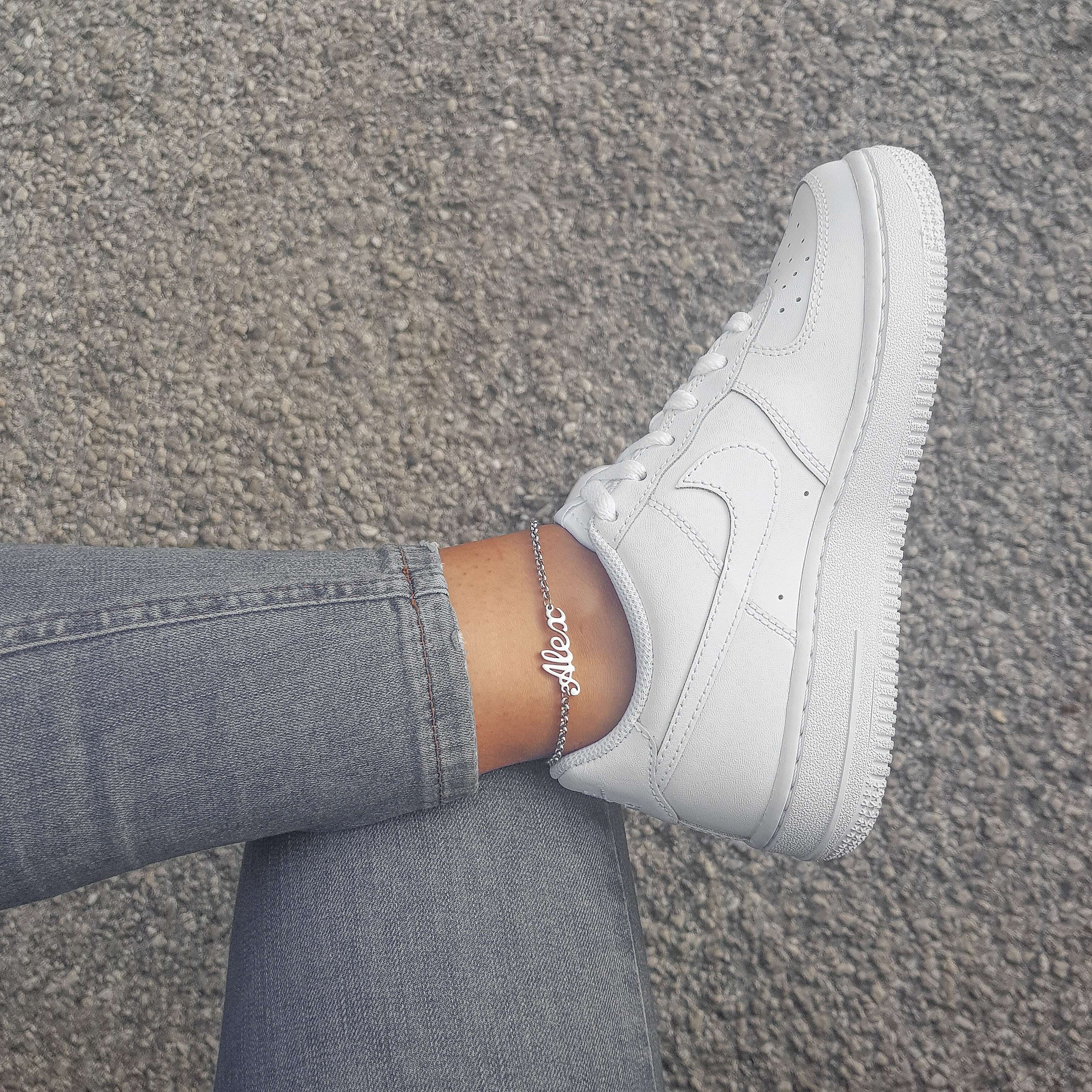 Silver Miami customised name anklet worn by a woman wearing light jeans and white trainers